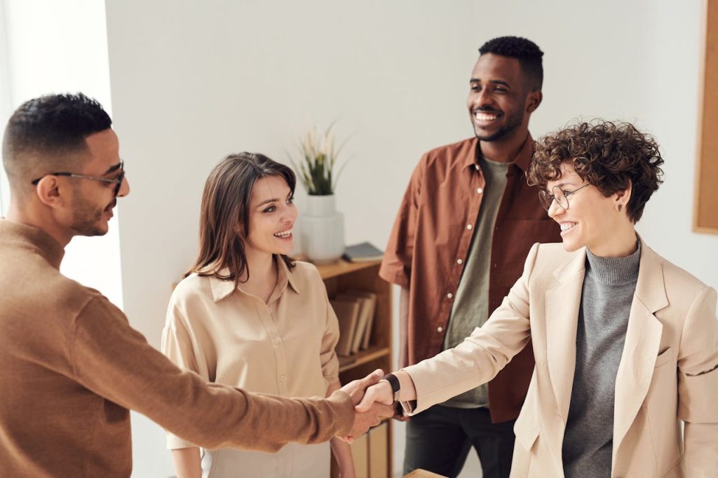 pexels-photo-3184416 Four colleagues smiling and shaking hands in a bright office setting.