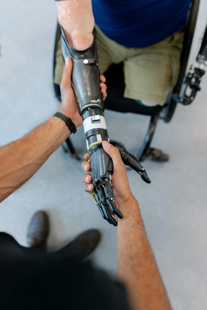 pexels-photo-3912979-3912979 Close-up of a man in a wheelchair with a prosthetic hand offering a handshake.